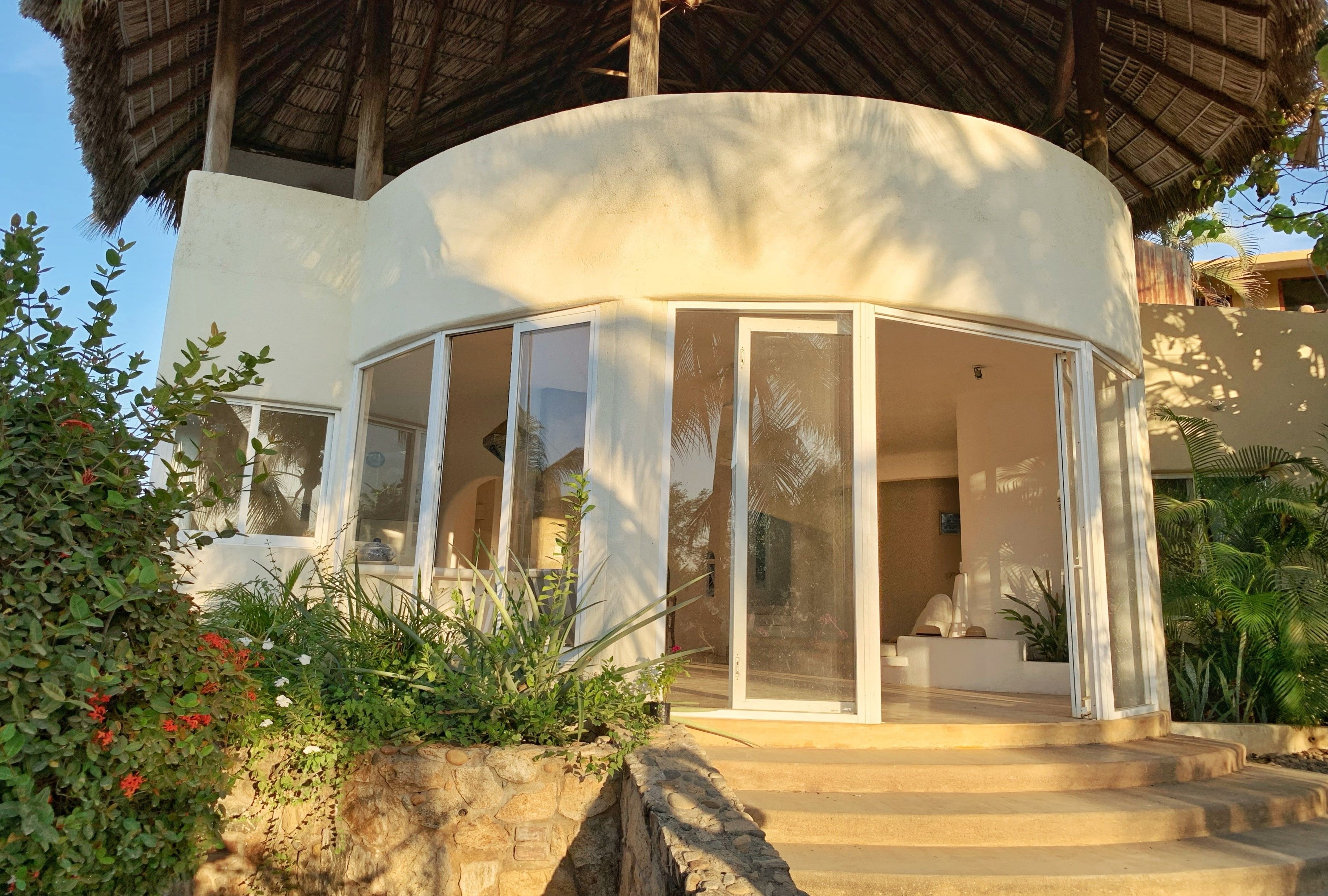 A curved building with a glass enclosure, stone steps, and tropical vegetation.