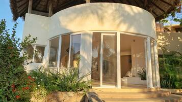 A curved building with a glass enclosure, stone steps, and tropical vegetation.