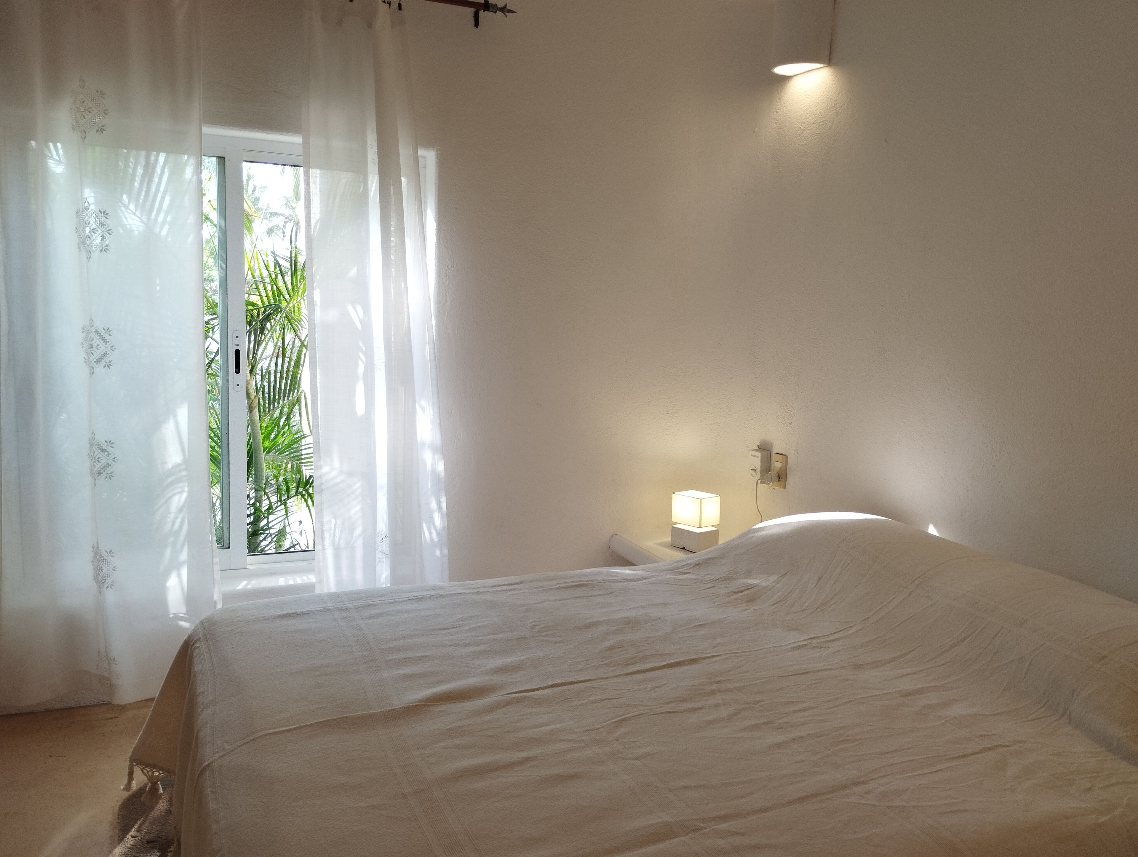 Quarto com cama, janela com cortinas leves e abajur.