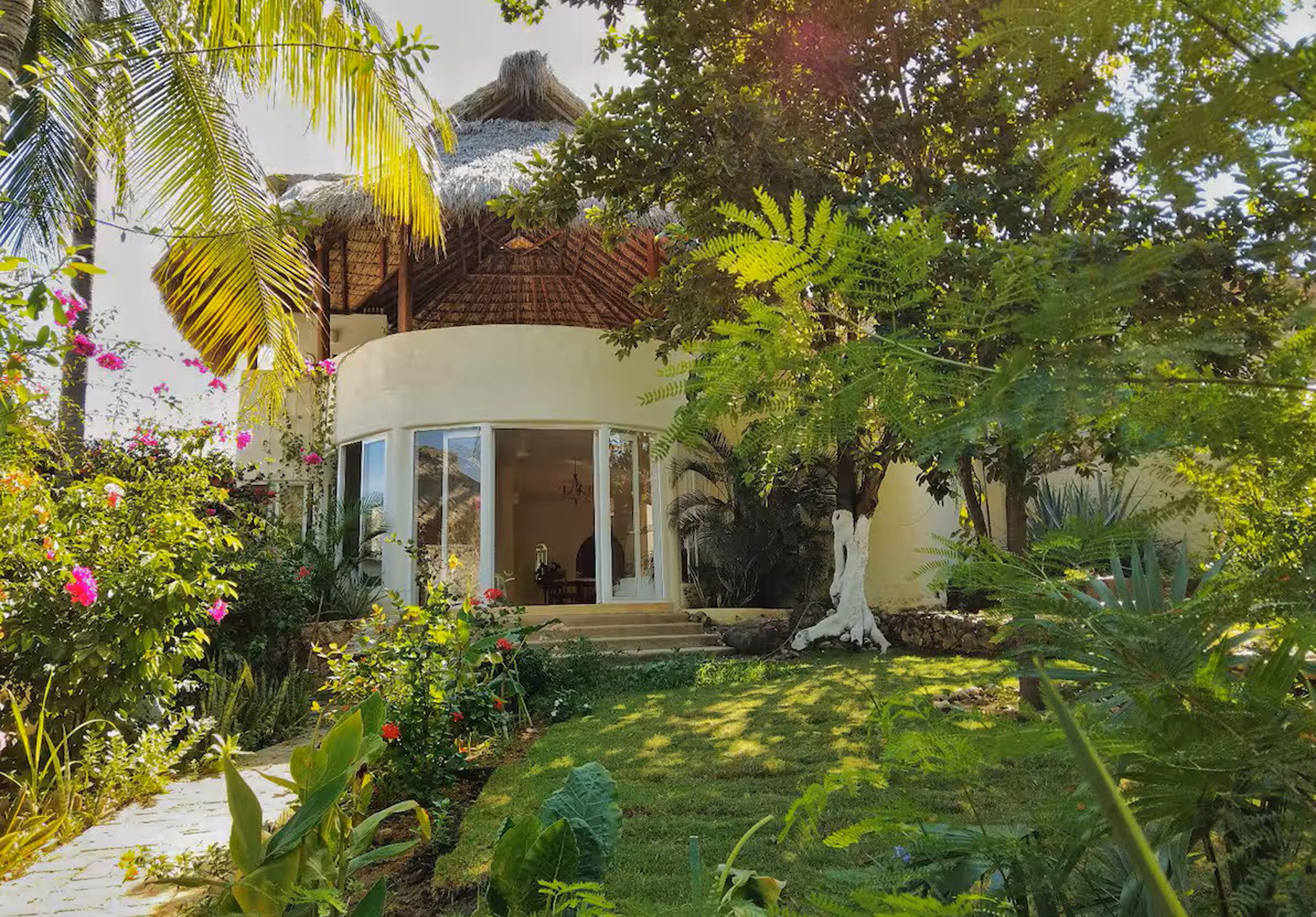 Una villa in stile tropicale con tetto di paglia, immersa nel verde rigoglioso e fiorita.