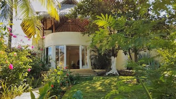 Una villa in stile tropicale con tetto di paglia, immersa nel verde rigoglioso e fiorita.