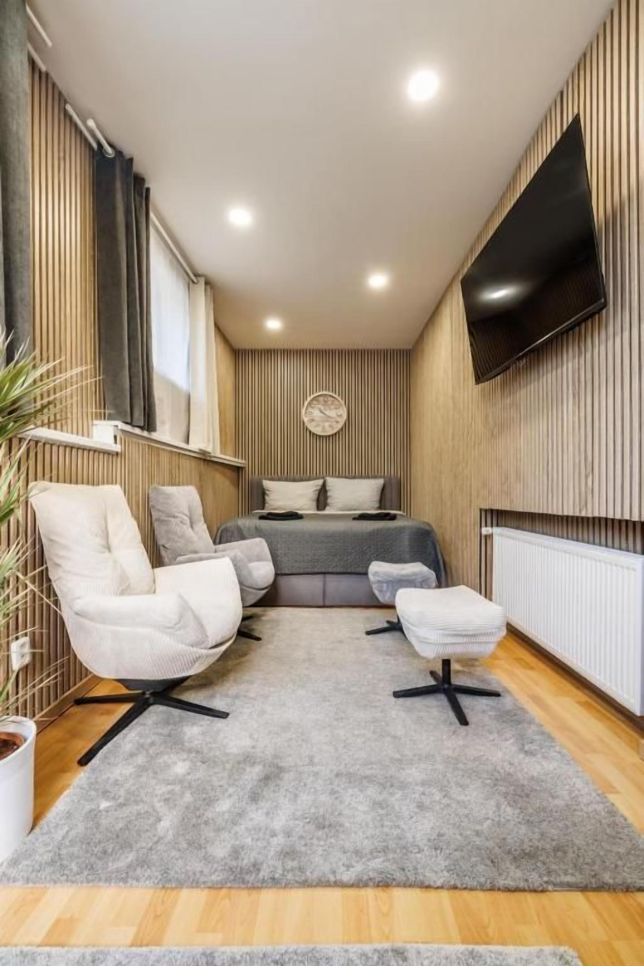 A modern bedroom with a bed, a TV, and a seating area with chairs and a rug.