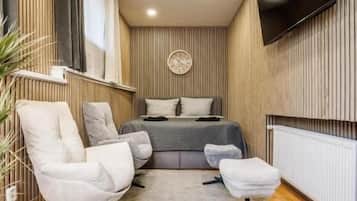 A modern bedroom with a bed, a TV, and a seating area with chairs and a rug.