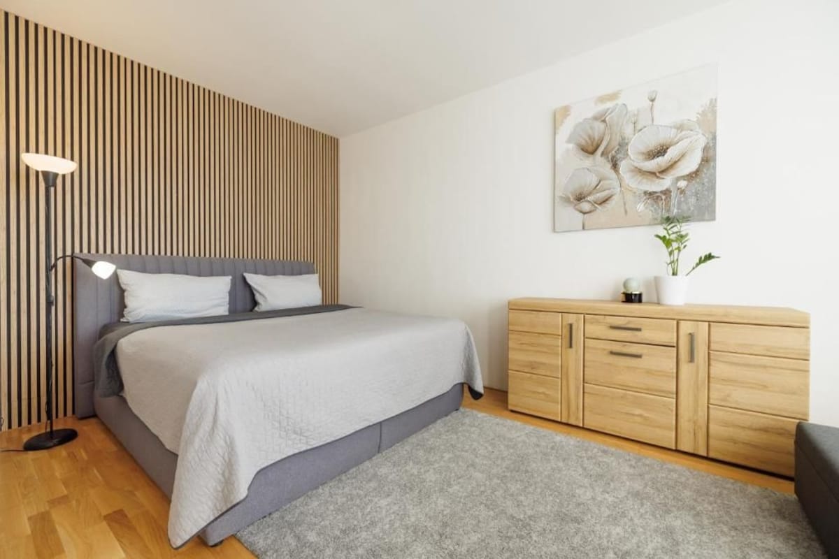 Quarto com cama, luminária de cabeceira, painel de parede de madeira e uma pintura.