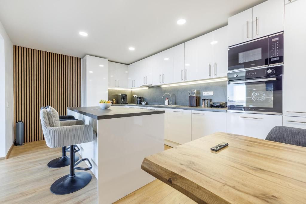 Une cuisine moderne avec des meubles blancs, une table à manger en bois et un coin bar avec des tabourets.