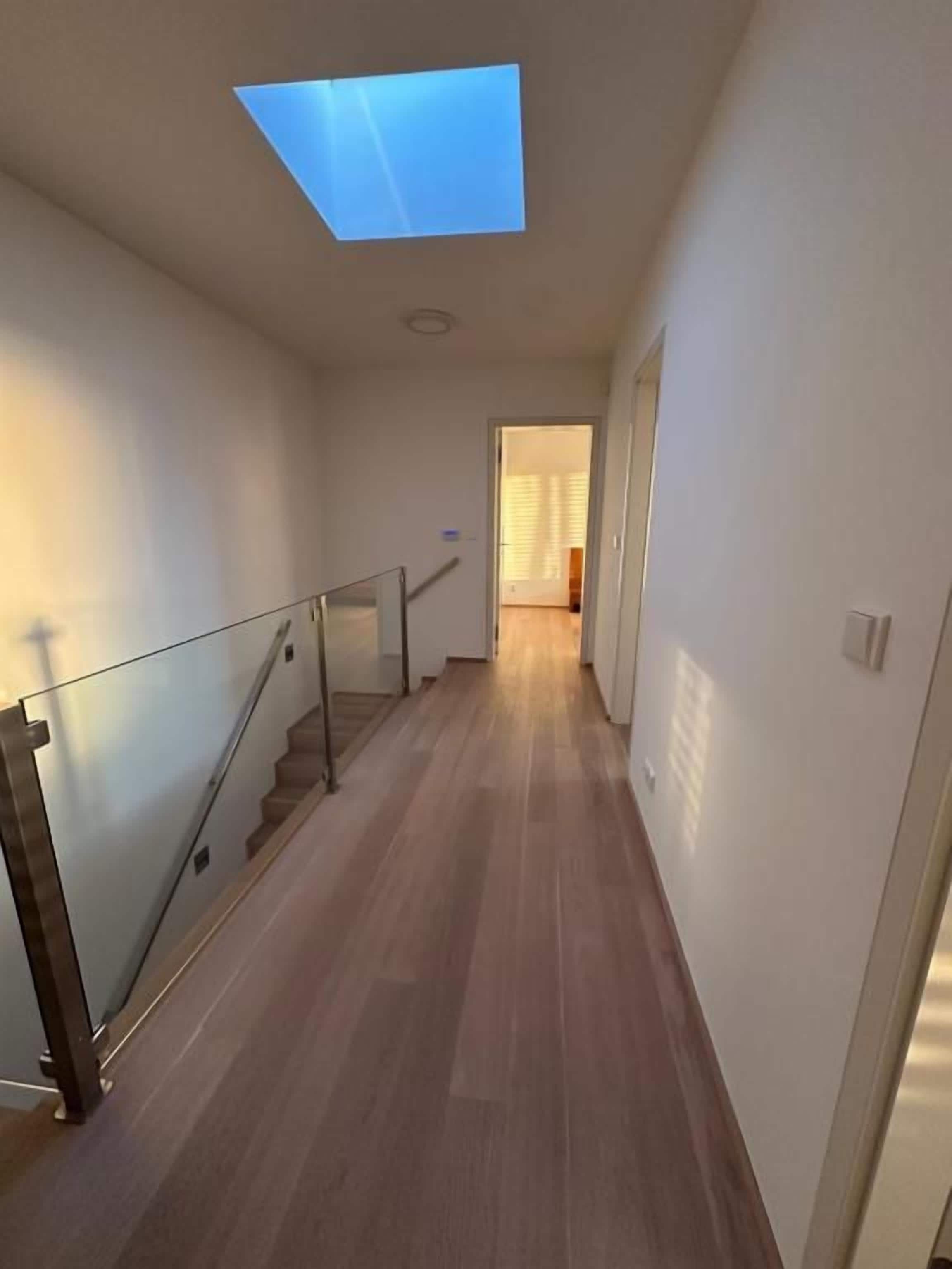 Un couloir doté d’une verrière, d’un plancher en bois et d’une rambarde en verre.