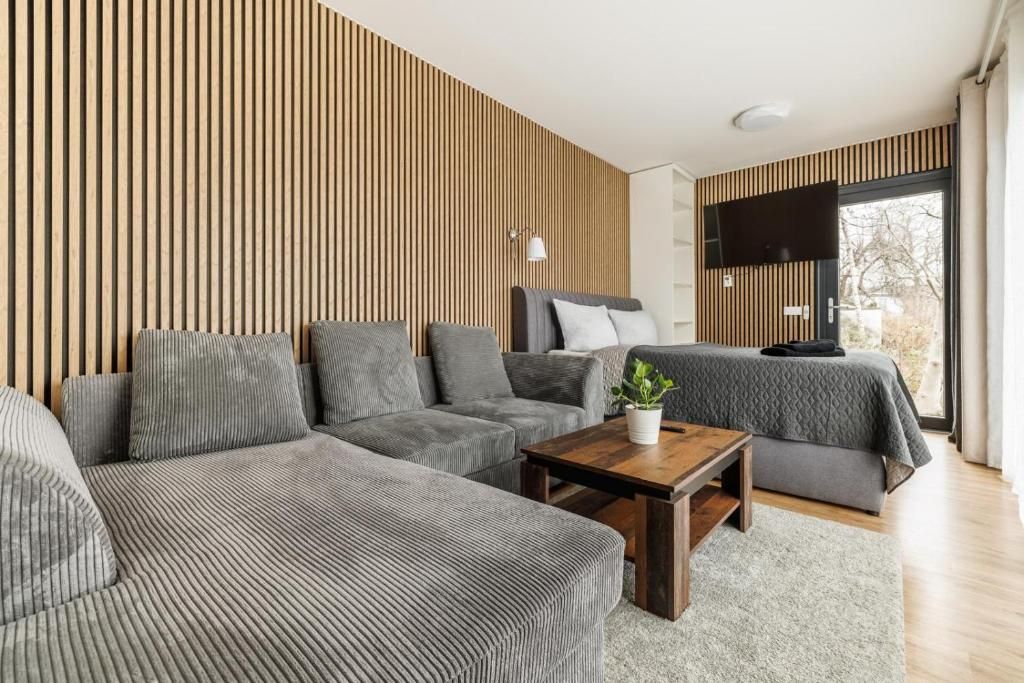 Un salon moderne avec un canapé d’angle, une petite table basse et un lit recouvert d’une couverture grise.