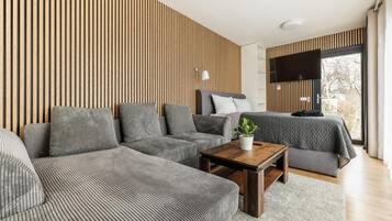 Un salon moderne avec un canapé d’angle, une petite table basse et un lit recouvert d’une couverture grise.