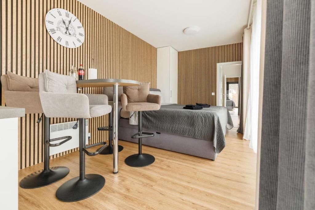A modern room with a bed, two bar stools, a round table, and a wall clock.