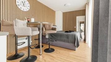 A modern room with a bed, two bar stools, a round table, and a wall clock.