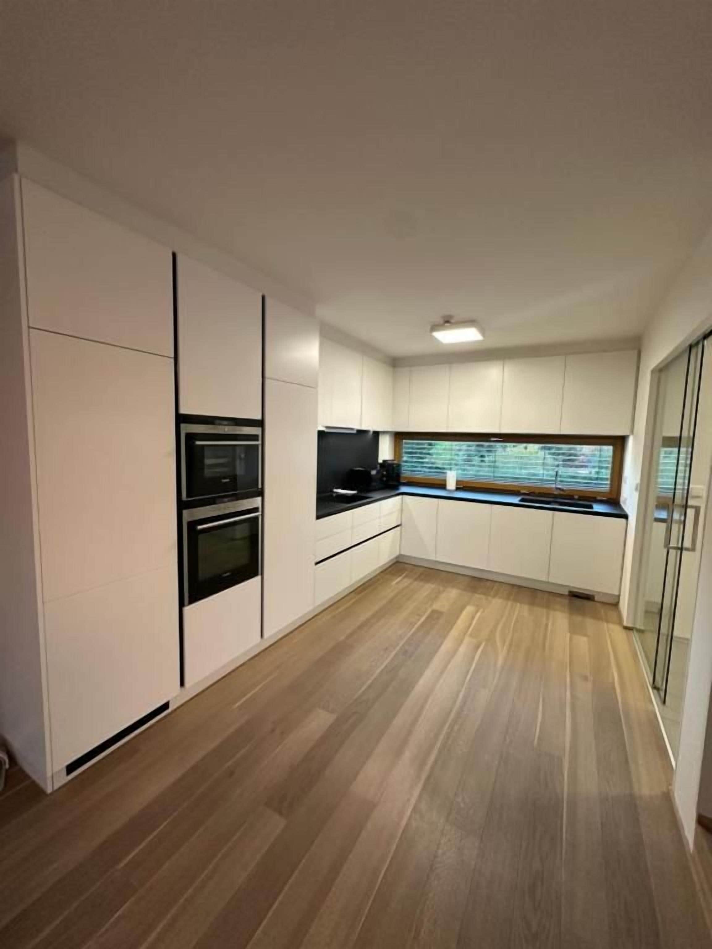 A modern kitchen with white cabinetry, a built-in oven, and a window with blinds.