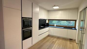 A modern kitchen with white cabinetry, a built-in oven, and a window with blinds.