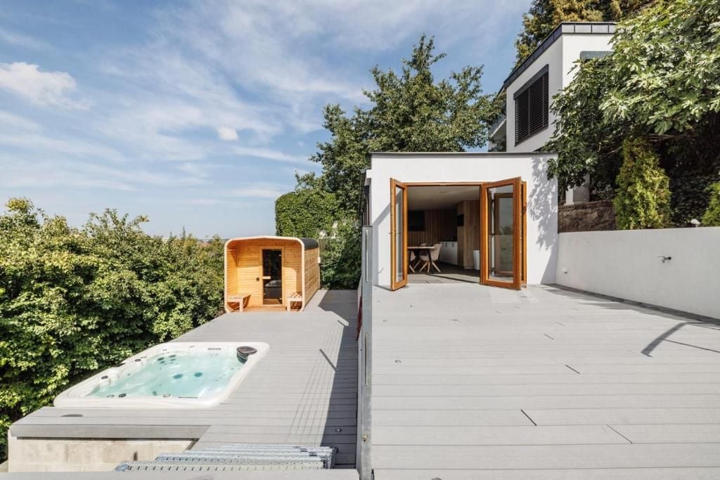 A modern outdoor deck with a hot tub, a wooden structure, and a glass door leading to a patio area.