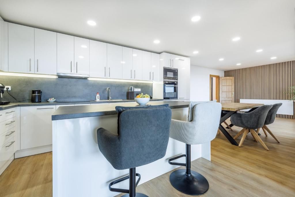 Een moderne keuken met witte kasten, een centraal eiland met barkrukken en een eethoek met een houten tafel en stoelen.