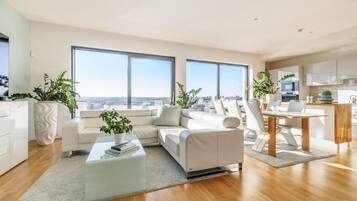 Una sala de estar moderna con un sofá, una mesa de centro y vistas de la ciudad a través de amplios ventanales.