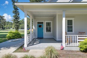 A white house with a blue door, a covered porch, and a small garden with an American flag. - Brand-New Cottage Minutes to Lake Marion & Golf (Summerton)
