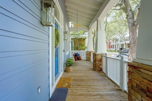 A covered porch with a wooden floor, a blue door, and a white railing.