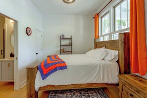 Un dormitori amb un llit, un panell de fusta al capçal, una tauleta de nit, una safata de nit, una prestatgeria i una finestra amb cortines.
