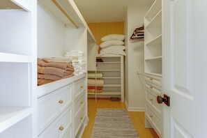 A narrow walk-through closet with shelves and drawers, containing folded towels and blankets. - FUN Luxury Haile Home w/ Hot Tub - Near UF (Gainesville)