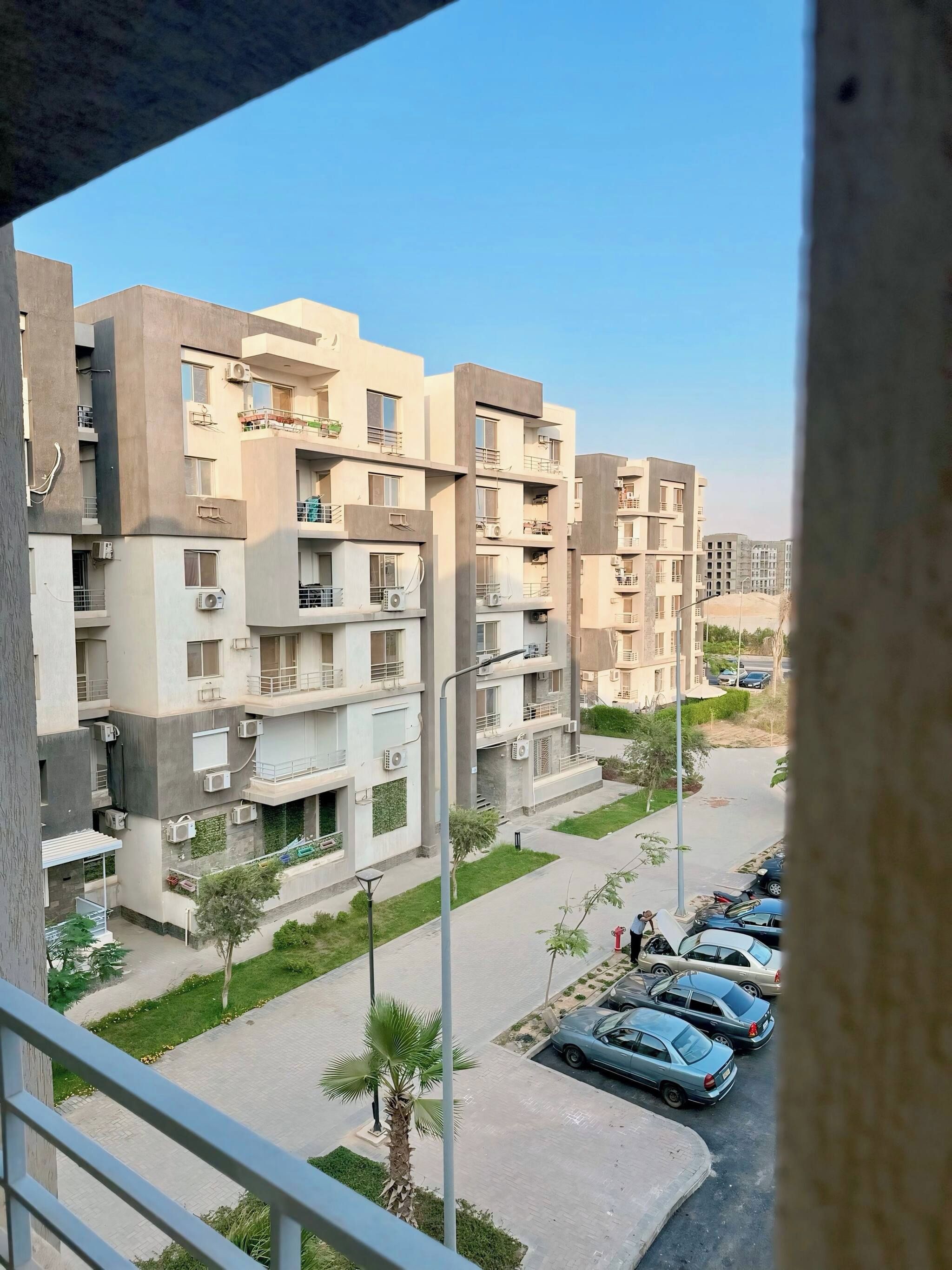 A residential building with multiple floors, balconies, and a parking area with cars.