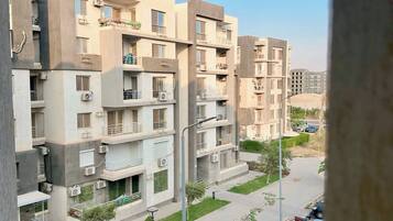A residential building with multiple floors, balconies, and a parking area with cars.