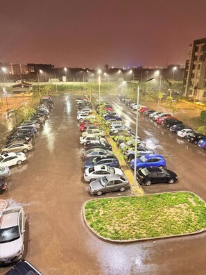 Un parking avec plusieurs rangées de voitures garées, éclairé par des lampes suspendues.