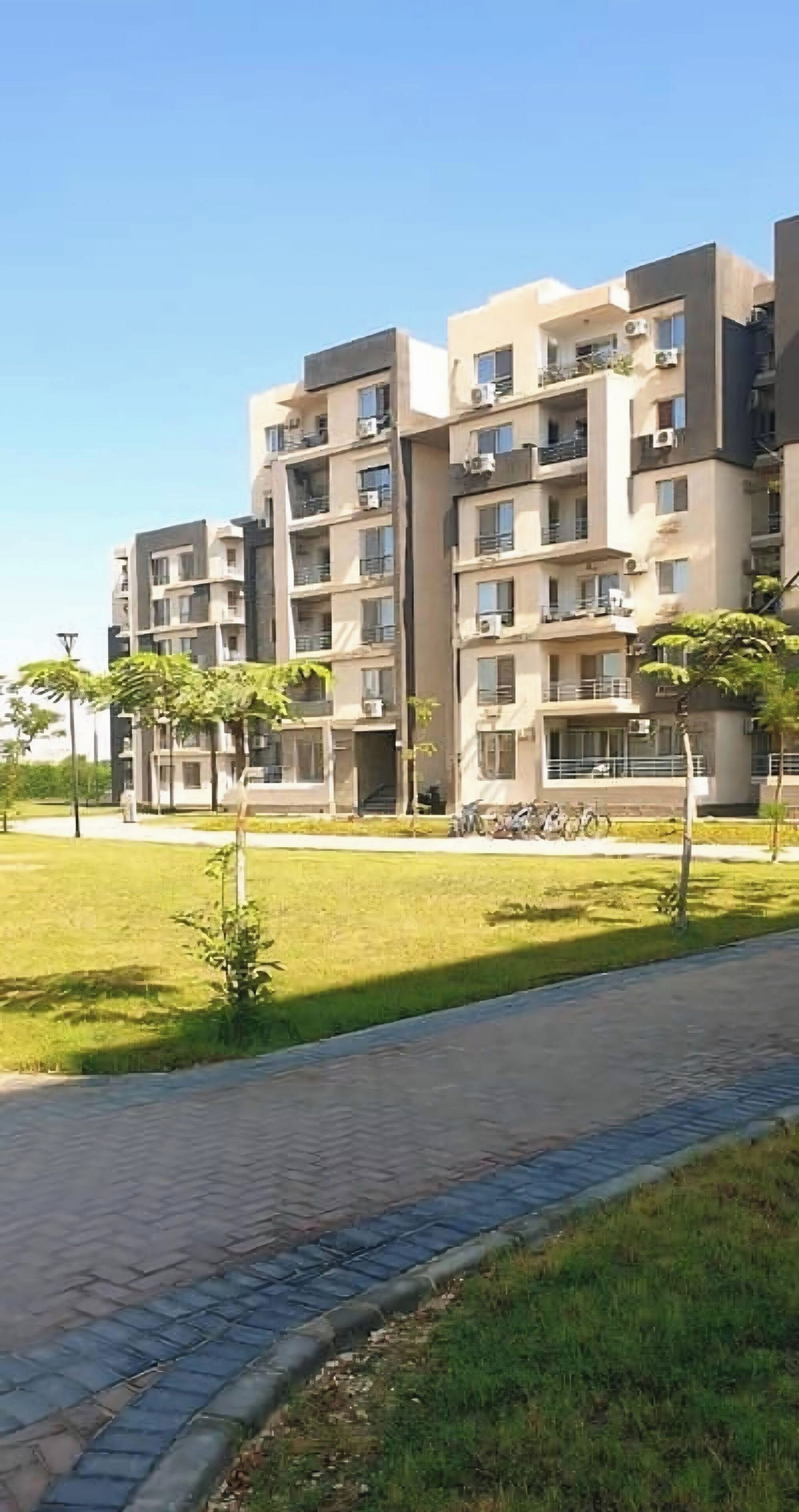 A multi-story residential building with balconies, air conditioning units, and a paved walkway.
