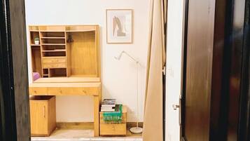 A room with a wooden desk, a standing lamp, a framed picture on the wall, and a wardrobe.