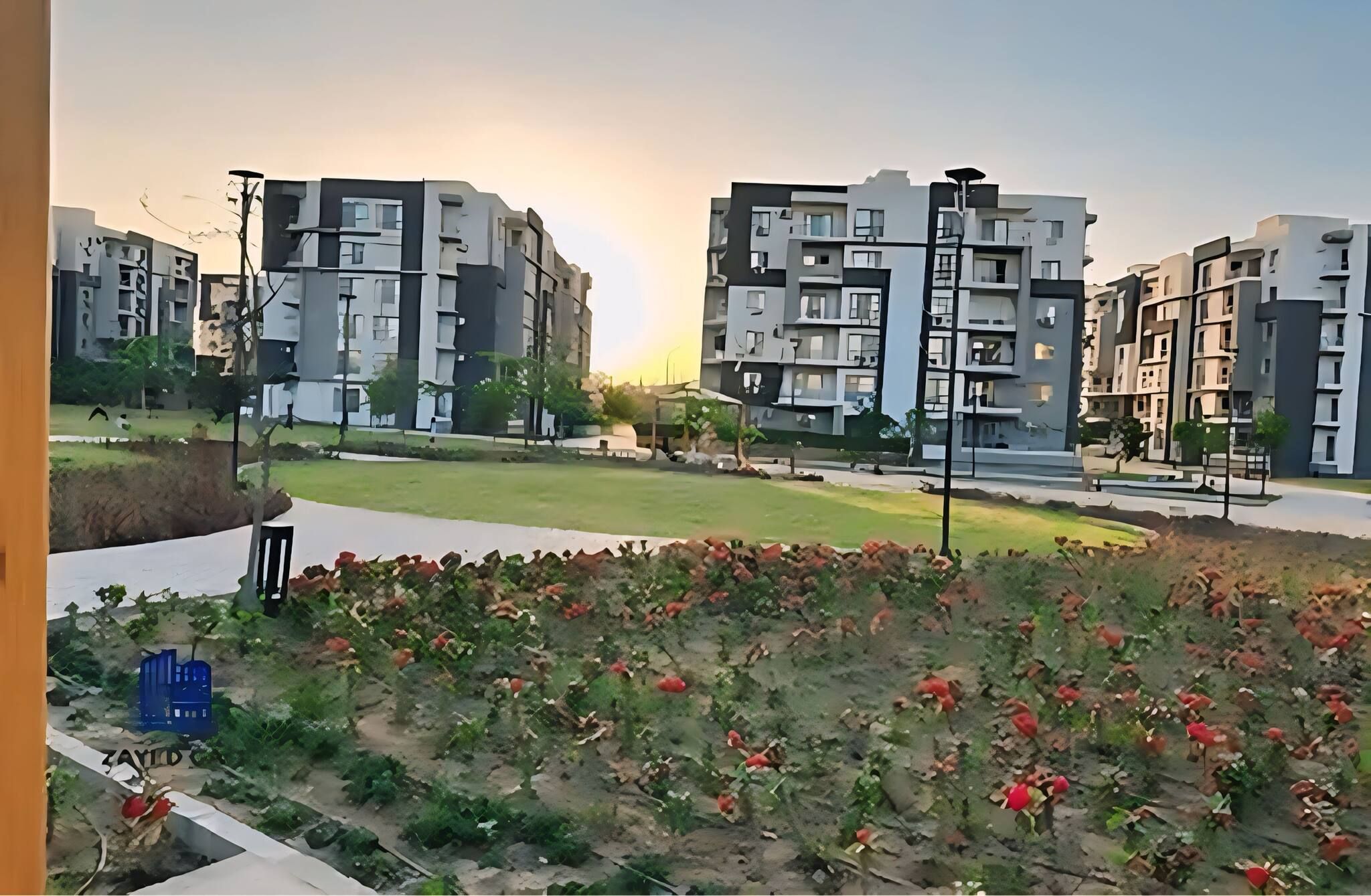 A residential area with modern apartment buildings, a grassy field, and a paved walkway.