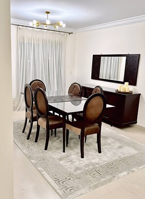 Un coin repas comprenant une table ronde, six chaises, un buffet en bois foncé et un lustre.