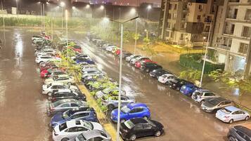 Un estacionamiento nocturno con coches aparcados en filas, rodeado de edificios y farolas.