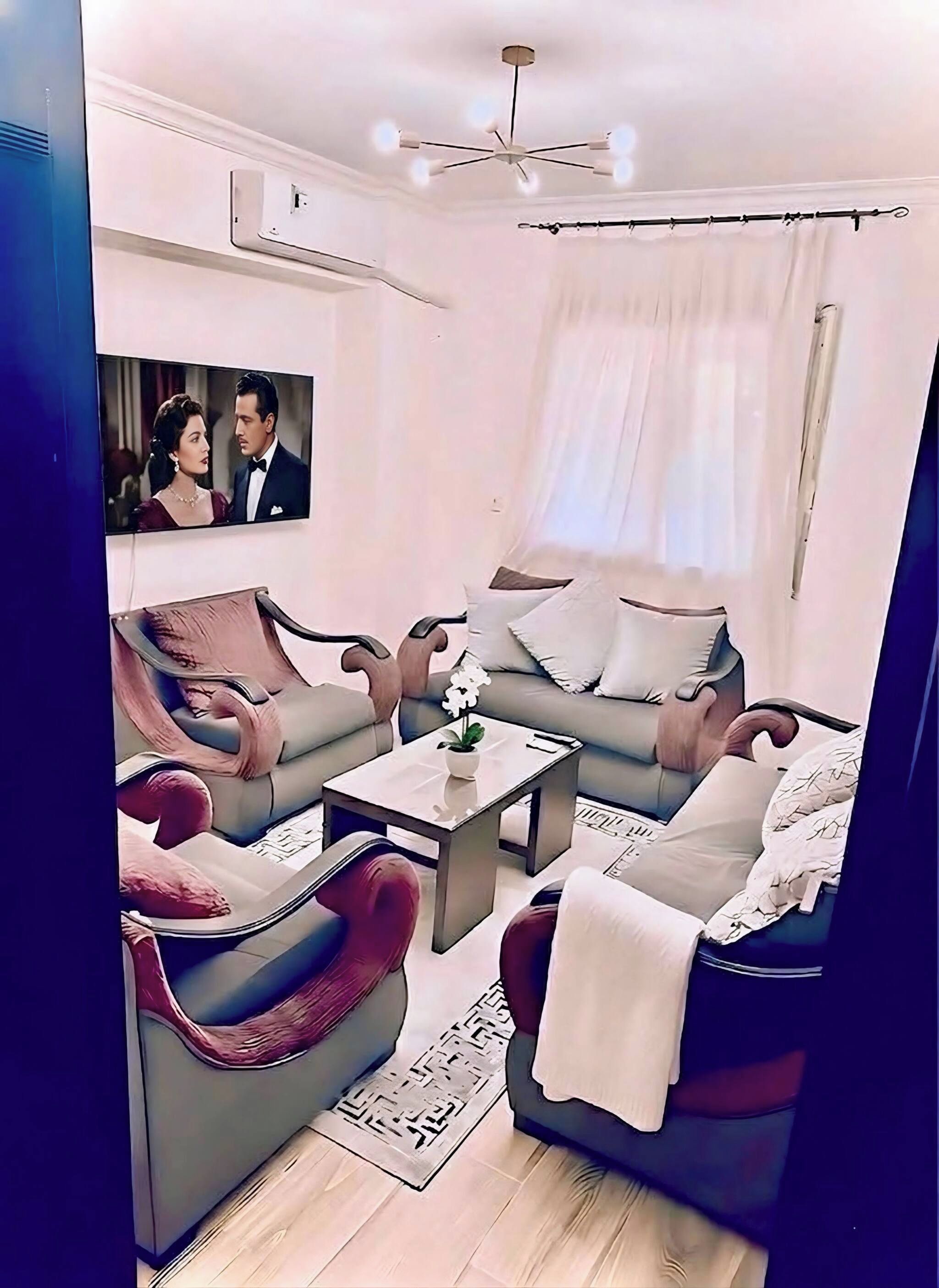 Ein modernes Wohnzimmer mit einer Couch, Sesseln, einem Couchtisch und einem an der Wand befestigten Fernseher.