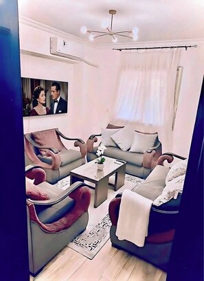 Ein modernes Wohnzimmer mit einer Couch, Sesseln, einem Couchtisch und einem an der Wand befestigten Fernseher.