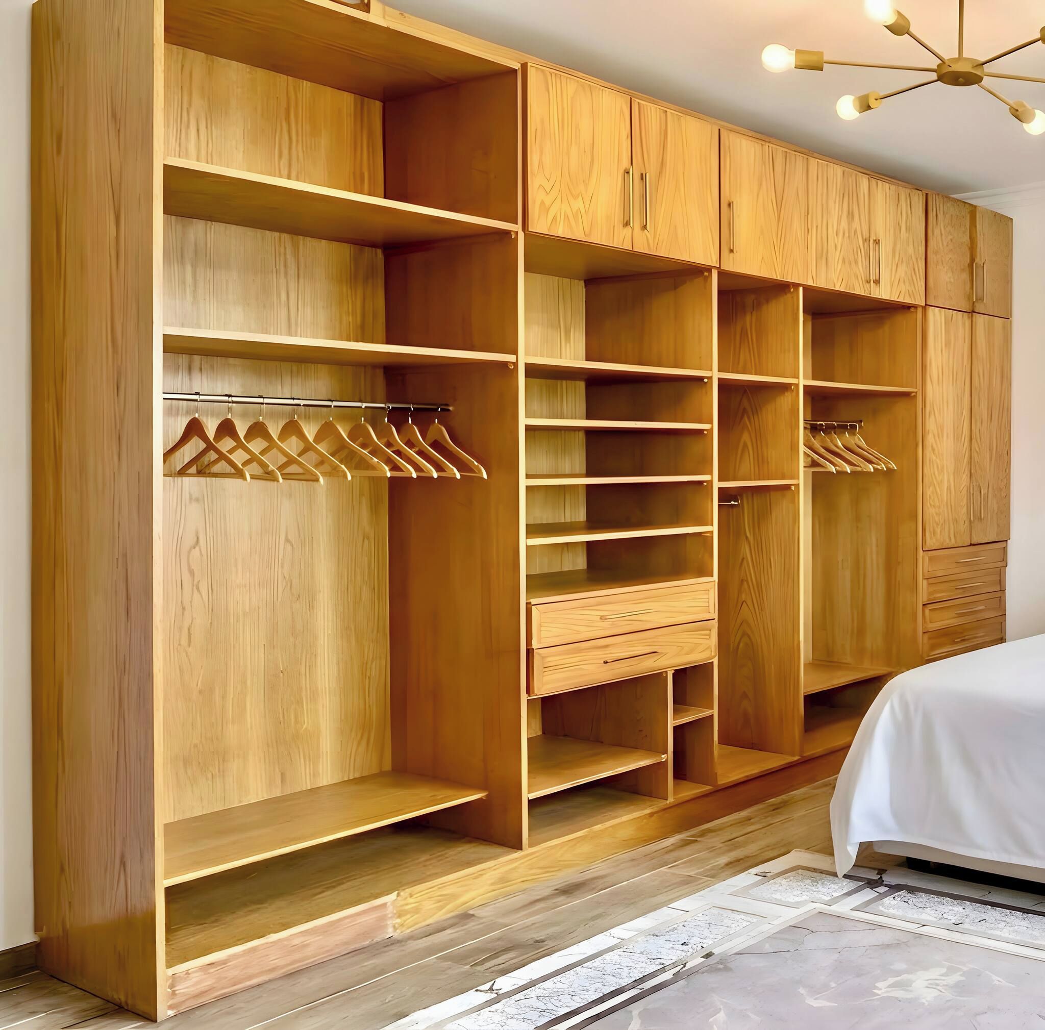 A wooden wardrobe with multiple shelves and hanging space, a bed with a white bedspread, and a modern ceiling light fixture.