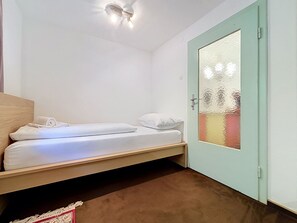 A single bed with a wooden headboard, a light-colored wall, and a door with frosted glass. - Ferienhaus Christl by Interhome (Pians)