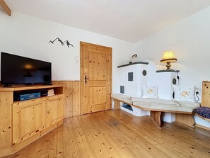 A cozy room with a wooden floor, a television on a wooden stand, a bench, a lamp, and a door with a small figurine on top. - Ferienhaus Christl by Interhome (Pians)