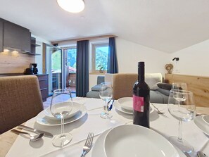Un coin repas avec une table dressée pour deux personnes, une bouteille de vin et une vue sur l’extérieur.