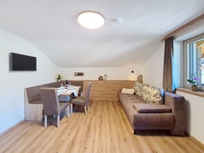 Et spiseområde med et bord dækket til fire personer, en sofa og et fjernsyn ophængt på væggen.