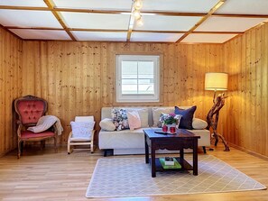 A room with wooden walls, a sofa, a chair, a table, and a lamp. - Huus 115 by Interhome (Dalaas)