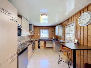 A kitchen with wooden cabinets, a countertop, a sink, a stove, and a clock on the wall. - Huus 115 by Interhome (Dalaas)