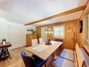 A wooden-paneled room with a dining table, chairs, a bench, and a hanging light fixture. - Huus 115 by Interhome (Dalaas)