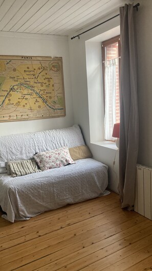 Une pièce avec un lit, une carte accrochée au mur, une fenêtre avec des rideaux et un radiateur.