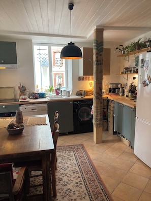 A kitchen with a washing machine, a dining table, and a hanging light fixture.