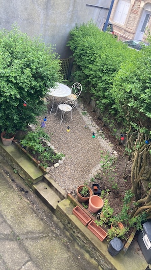 Un espace jardin aménagé avec une table et des chaises, entouré de plantes en pot et bordé d’un chemin de gravier.