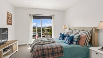 A bedroom with a bed, a television, a window with curtains, and a view of the outdoors.