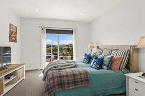 A bedroom with a bed, a television, a window with curtains, and a view of the outdoors. - Villa Vie: Spacious family escape in Warkworth near Matakana (Warkworth)