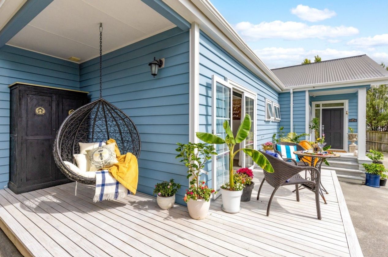 A porch with a hanging chair, potted plants, and outdoor furniture.