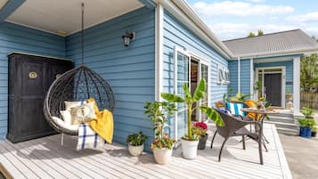 A porch with a hanging chair, potted plants, and outdoor furniture.