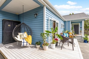 A porch with a hanging chair, potted plants, and outdoor furniture. - Villa Vie: Spacious family escape in Warkworth near Matakana (Warkworth)