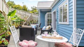 A patio with wicker furniture, a table with a tray of items, and a blue house in the background.